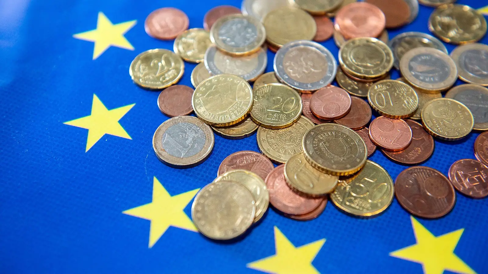 Monedas de euro sobre la bandera de la Unión Europea